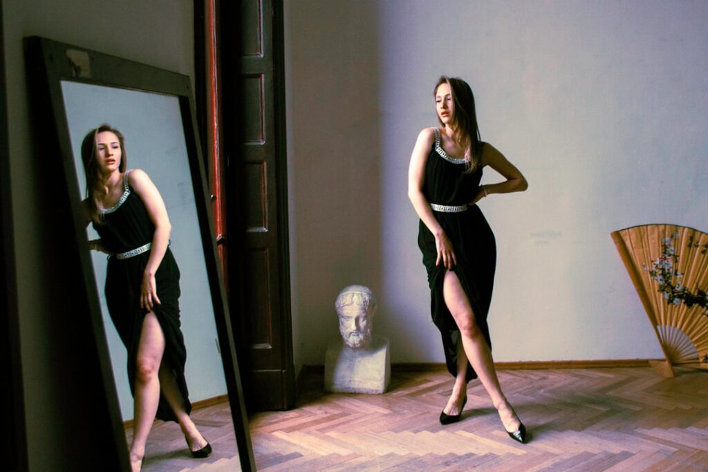 a woman in a black dress standing in front of a mirror