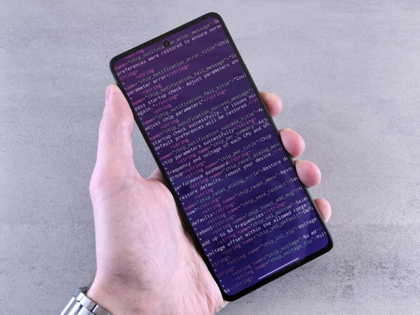 Hand holding smartphone displaying lines of code