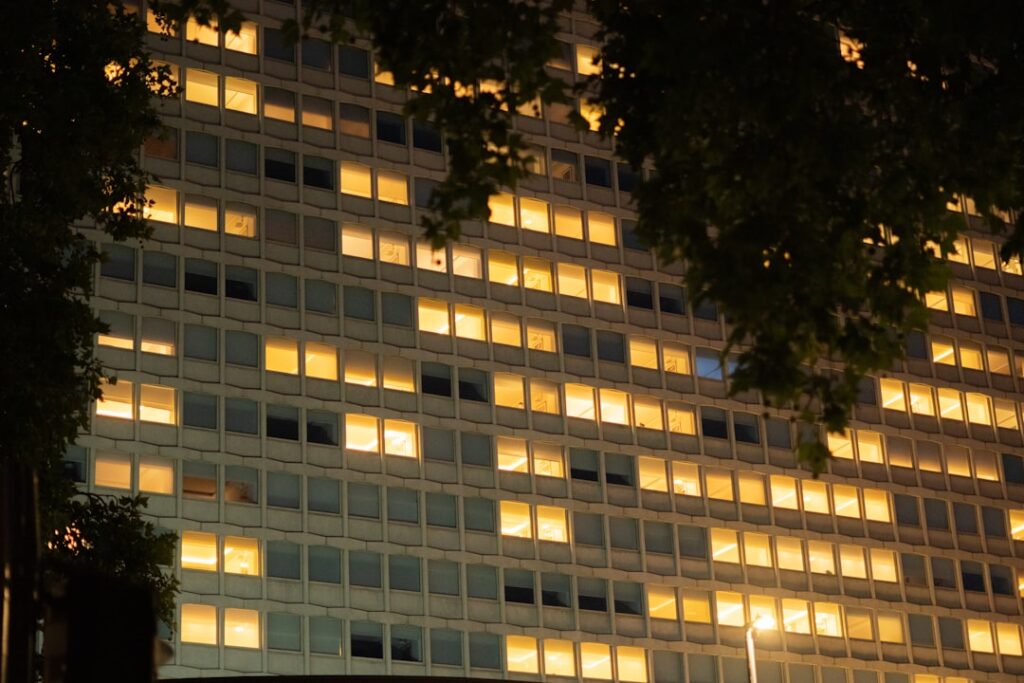 Illuminated office building windows at night, framed by trees.