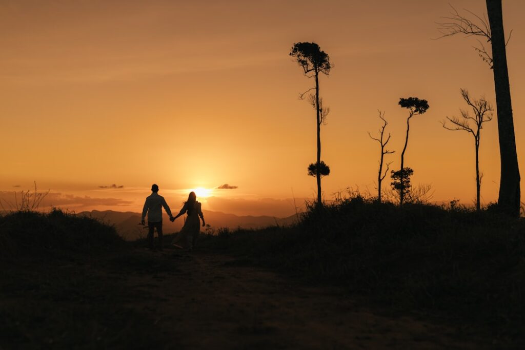 a man and a woman holding hands as the sun sets