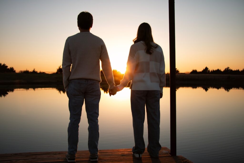 Couple holding hands watching sunset over lake