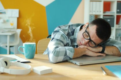 Man sleeping at desk with coffee and laptop.
