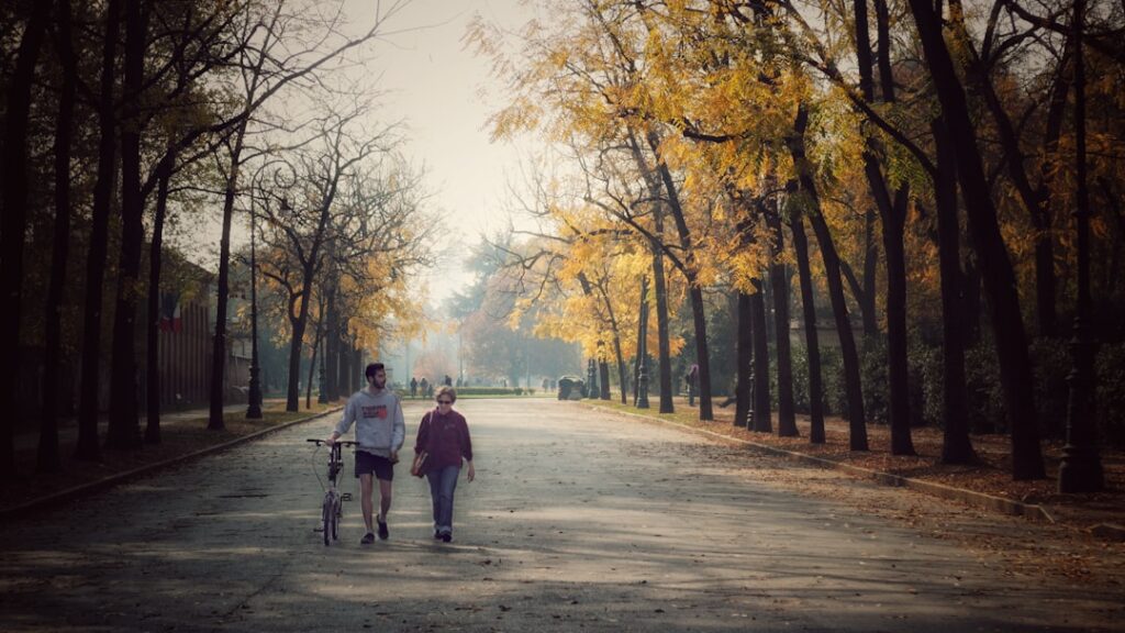 Couple walking dog on autumn park path.