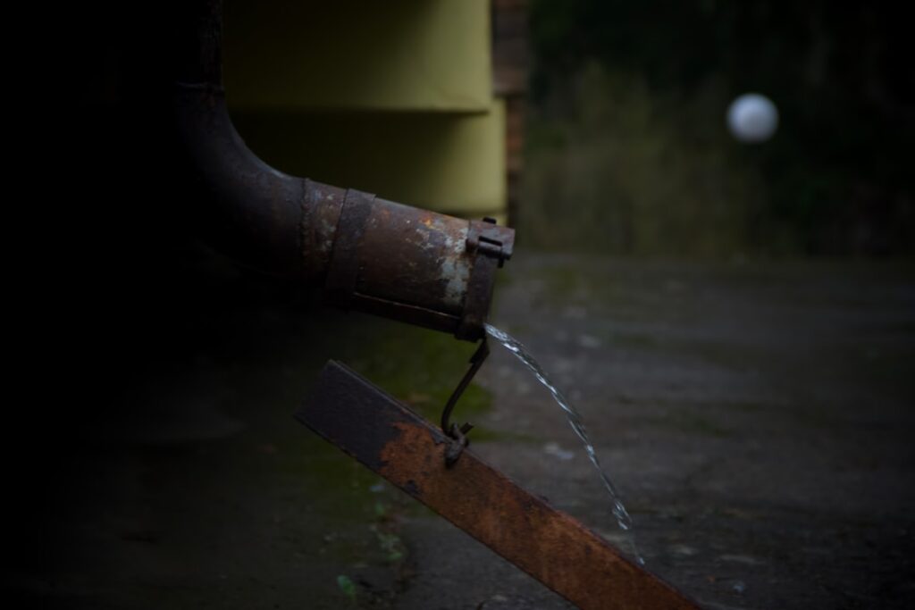 Water dripping from a rusty downspout onto a metal surface.