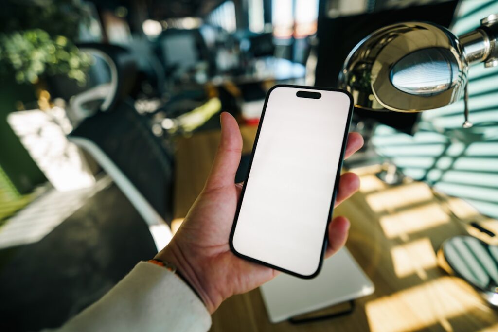 Hand holding a smartphone with a blank white screen.
