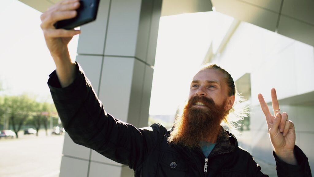 Man with beard takes a selfie, making peace sign.