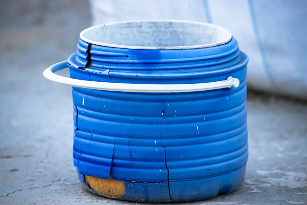 A damaged blue plastic barrel with a white handle.