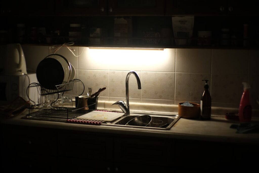 Kitchen sink area illuminated by under-cabinet lighting.