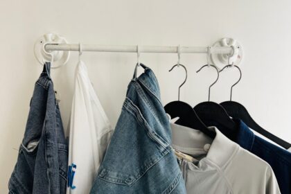 Clothes hang on a rack against a white wall.