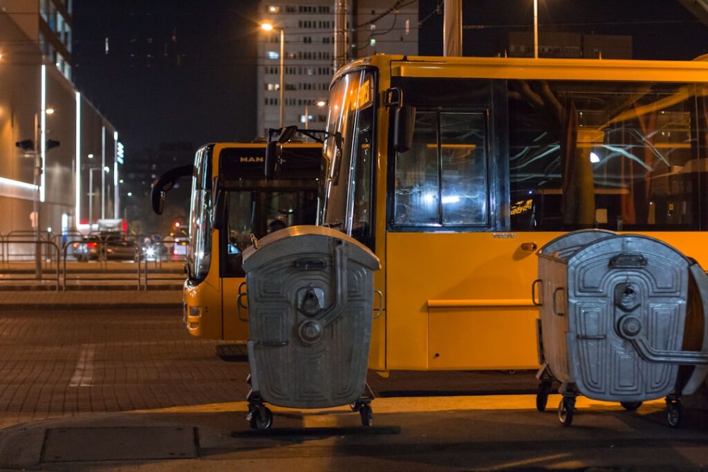 Buses are parked next to some garbage bins at night.