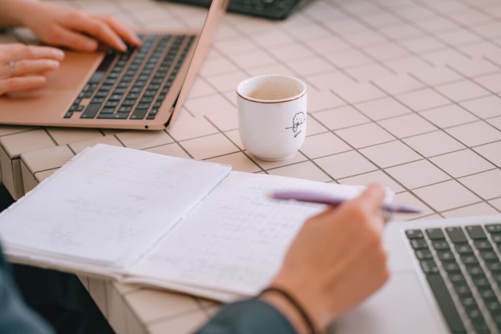 Two people working on laptops with notebook and coffee.