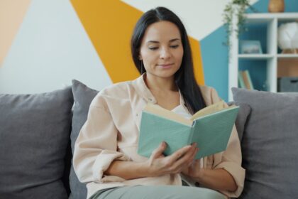 A woman reads a book while sitting on a couch.
