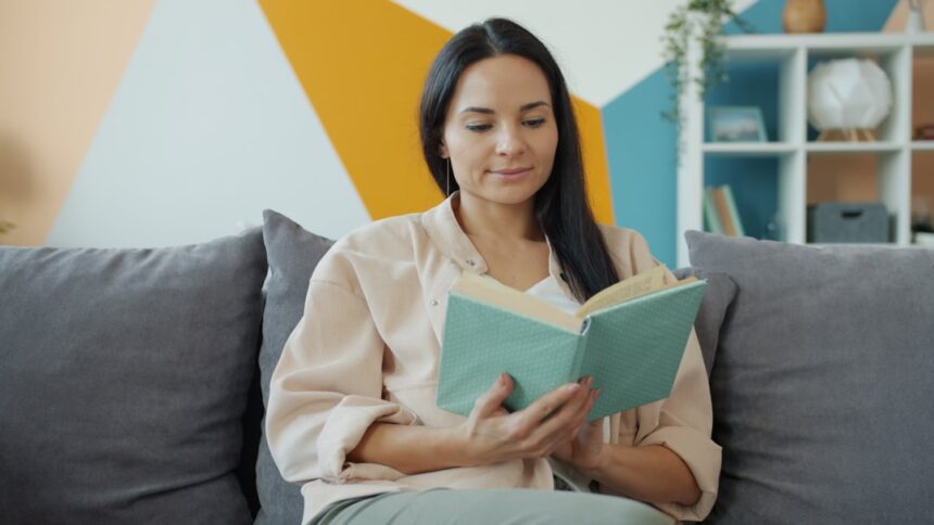 A woman reads a book while sitting on a couch.