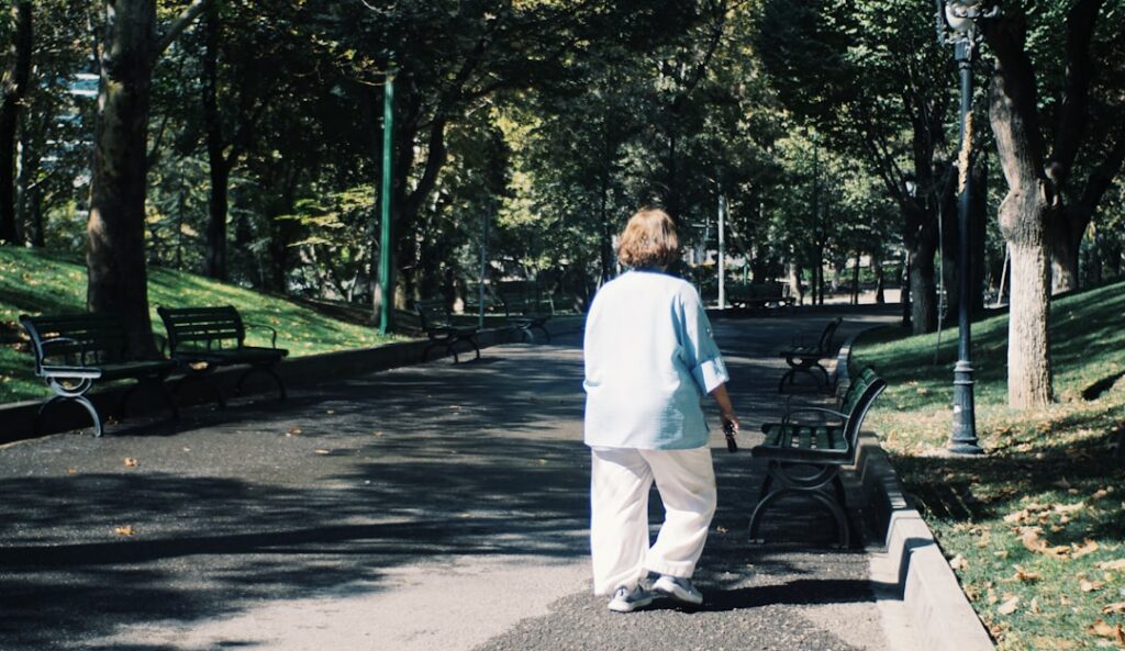 Woman walking down a park path surrounded by trees.