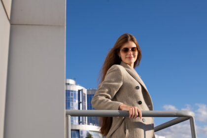 a woman in a coat and sunglasses leaning on a railing
