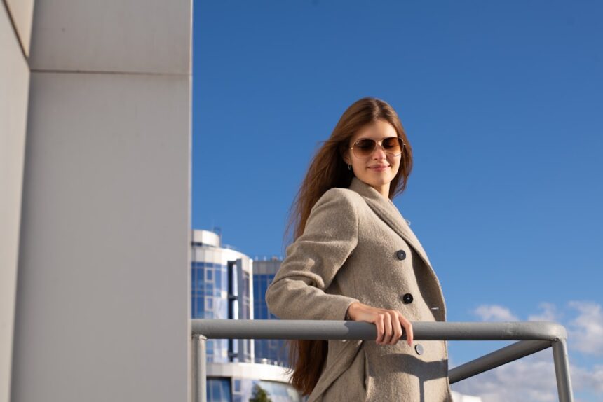 a woman in a coat and sunglasses leaning on a railing