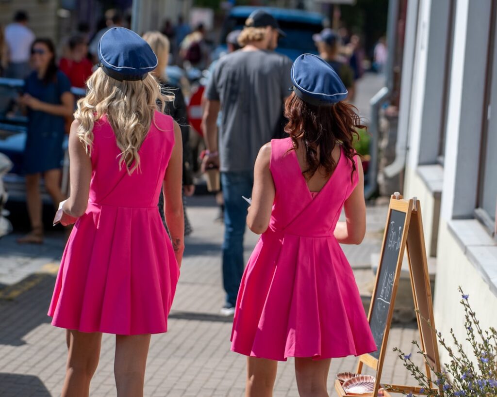Two women in pink dresses walk down a street