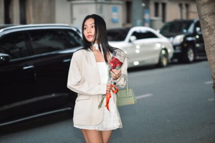a woman standing on the side of a street holding a bouquet of flowers