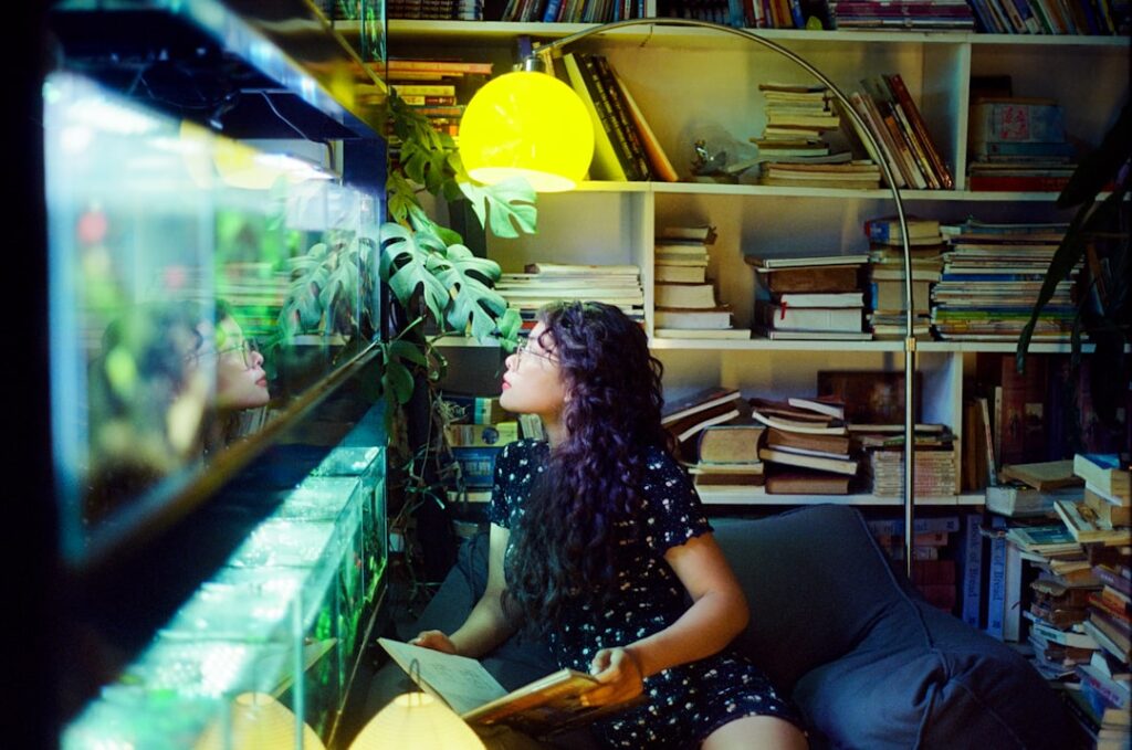 Woman reading book by aquarium with bookshelf and bookshelf