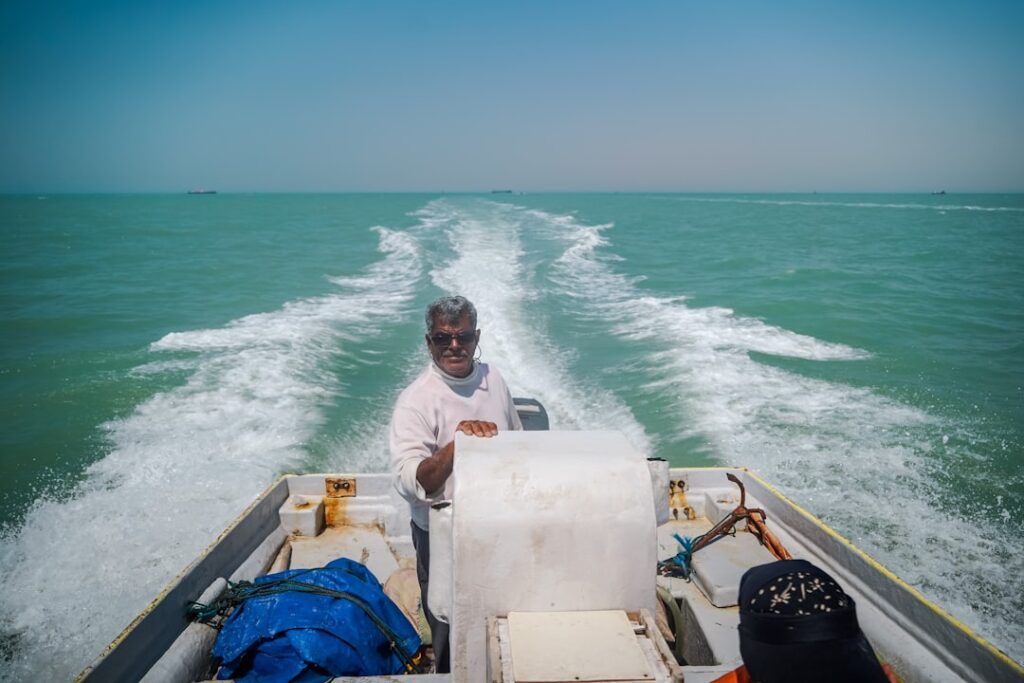 A man steers a boat on a sunny sea.