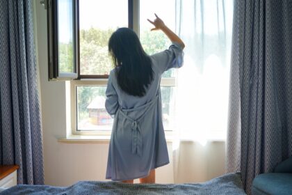 a woman standing in front of a window in a bedroom