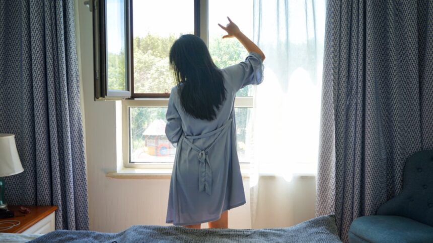 a woman standing in front of a window in a bedroom
