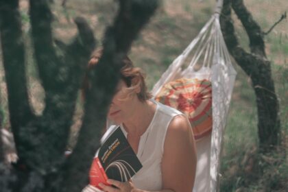 A woman sitting in a hammock reading a book
