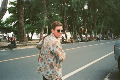 a person in a dress shirt on a street with trees and motorcycles
