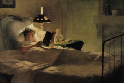 Woman reading in bed by lamplight