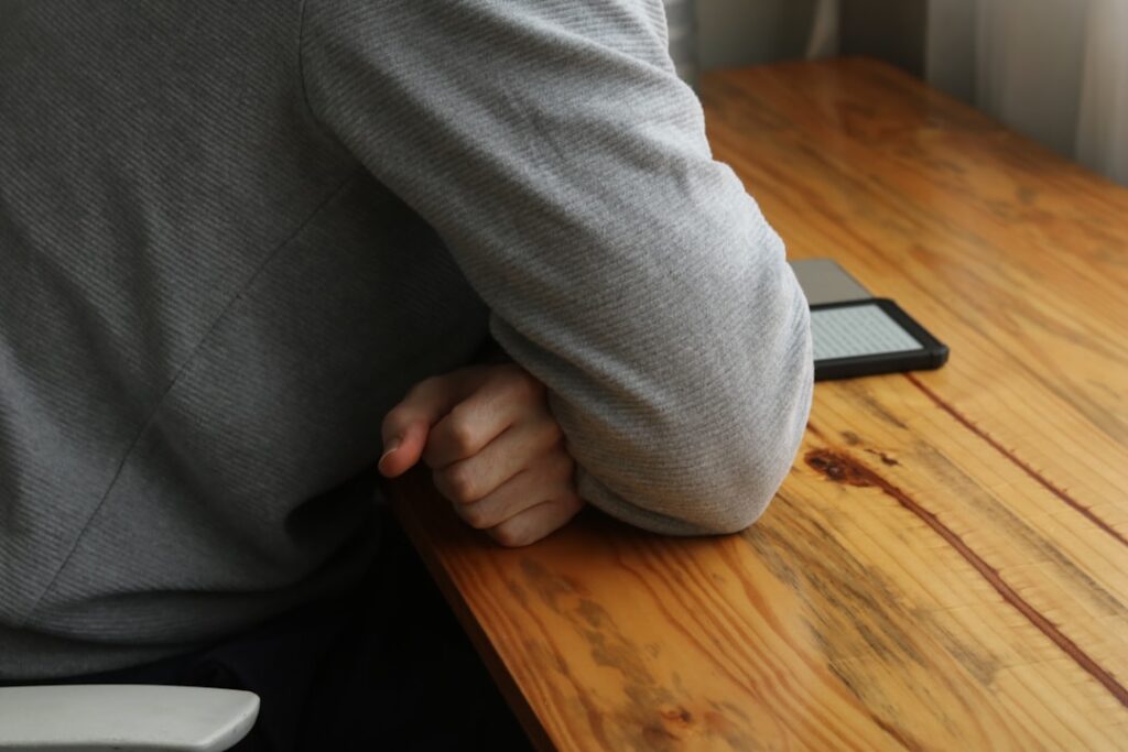 Person leans on a wooden table with their elbow.