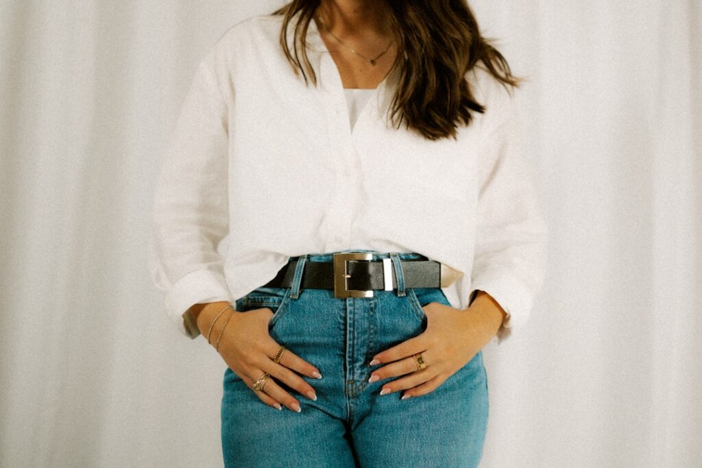 Woman wearing a white shirt, jeans, and a belt.