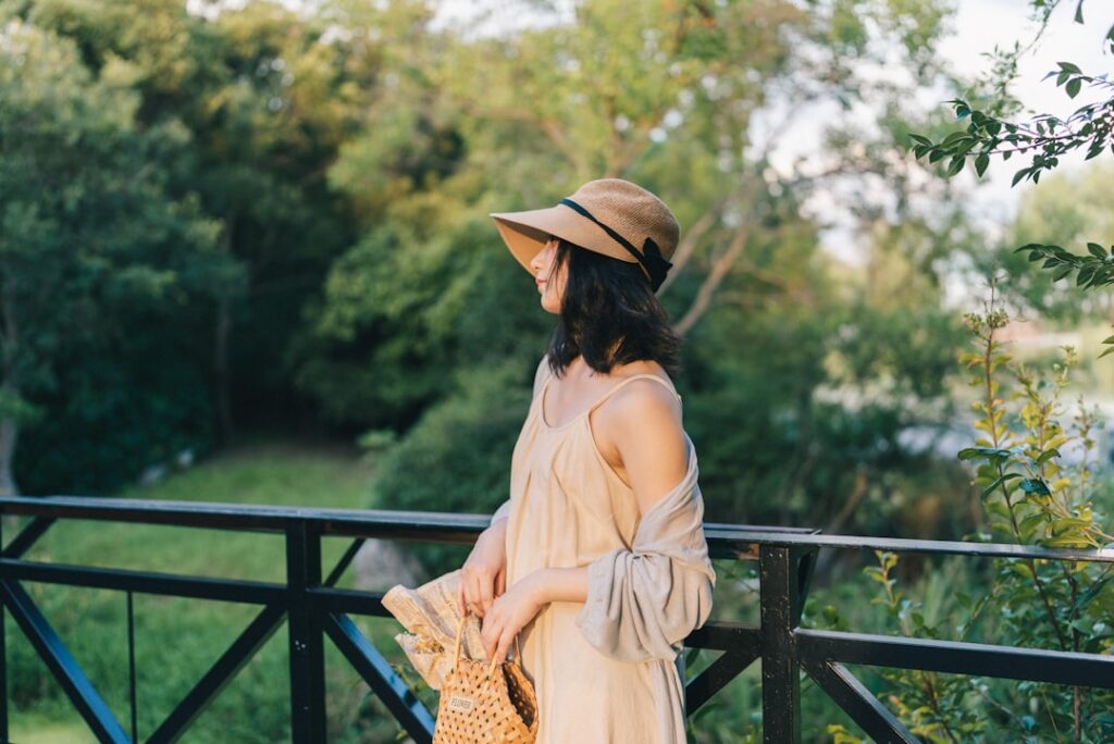 a woman in a hat and dress standing on a bridge