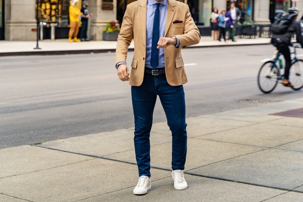 person in blue denim jeans and brown coat standing on sidewalk during daytime