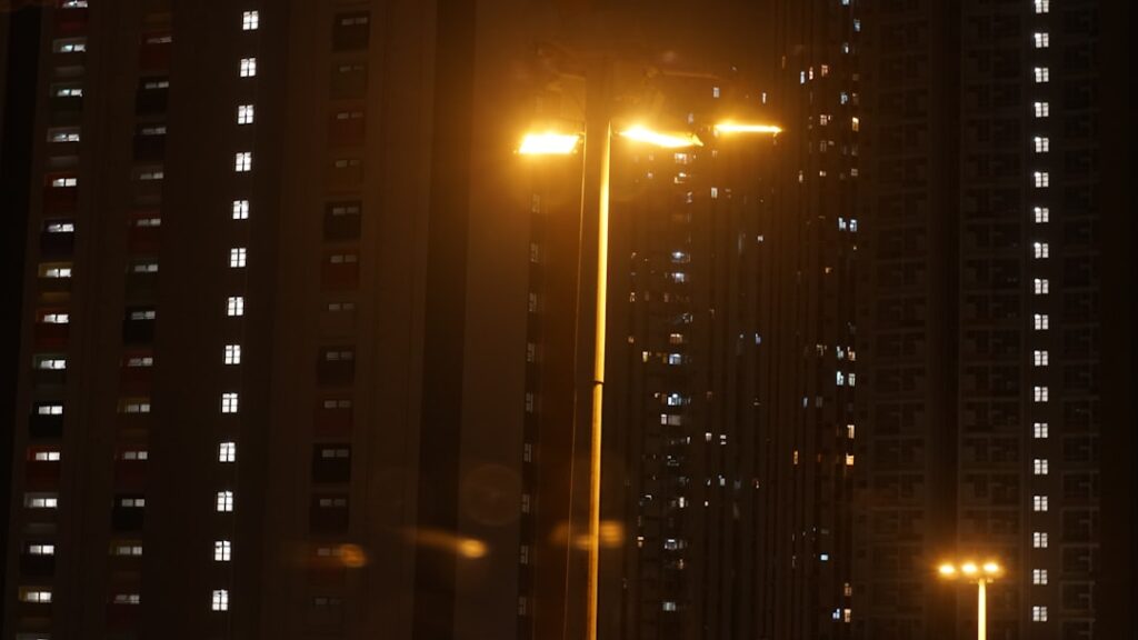 Streetlights illuminate apartment buildings at night.