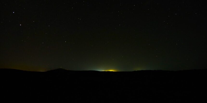 Stars shine over a distant city at night.