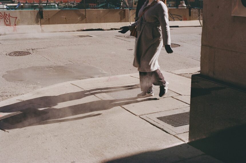 Person walking on a sidewalk casting long shadows.