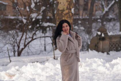 A woman in a coat stands in the snow.