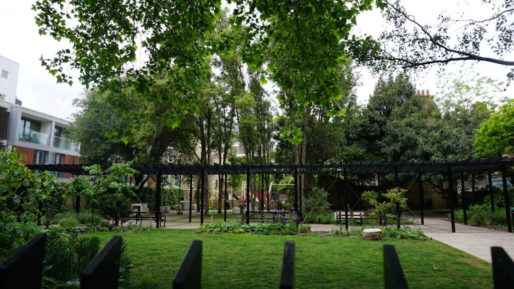 Urban park featuring green trees, grass, and dark pergolas.