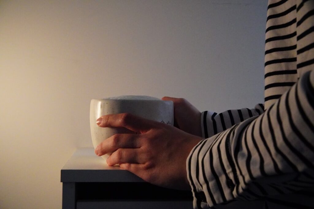 Hands holding a white mug on a table.
