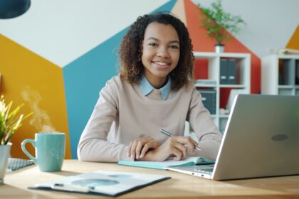 Young woman smiling at desk with laptop and coffee.