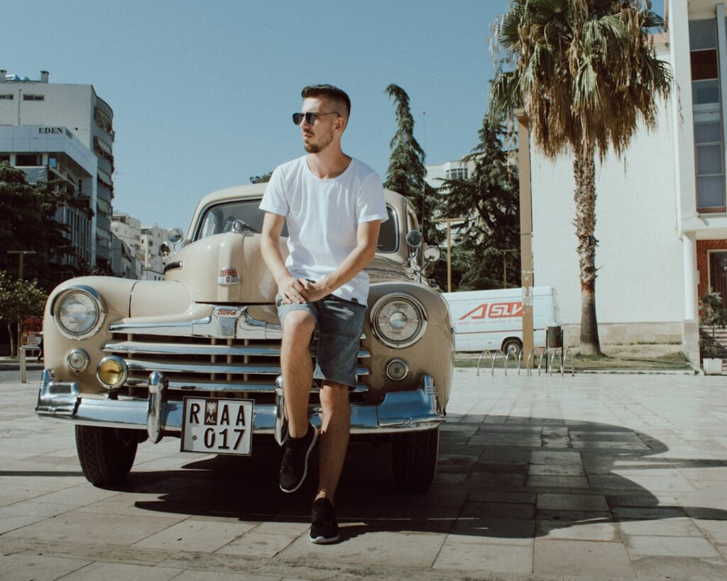 man in white crew neck t-shirt and blue denim shorts sitting on blue car