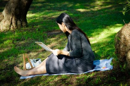 Woman reading tablet on blanket in grassy park.