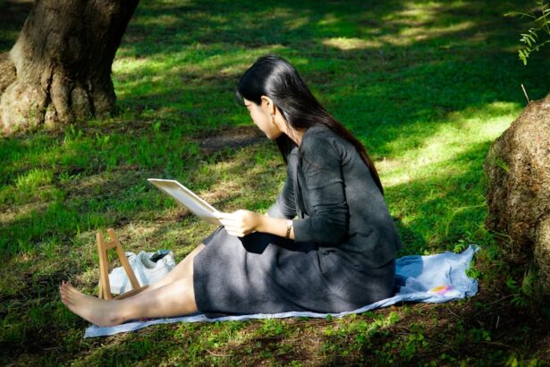 Woman reading tablet on blanket in grassy park.