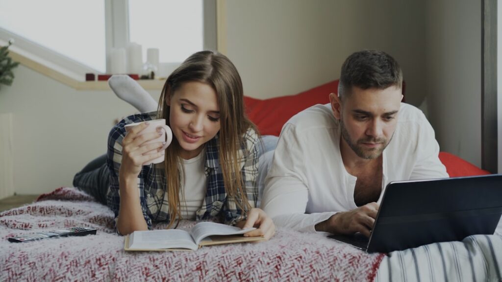 Couple relaxing on bed with book and laptop