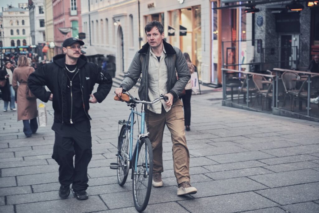 Two men walk with a bicycle on a city street.