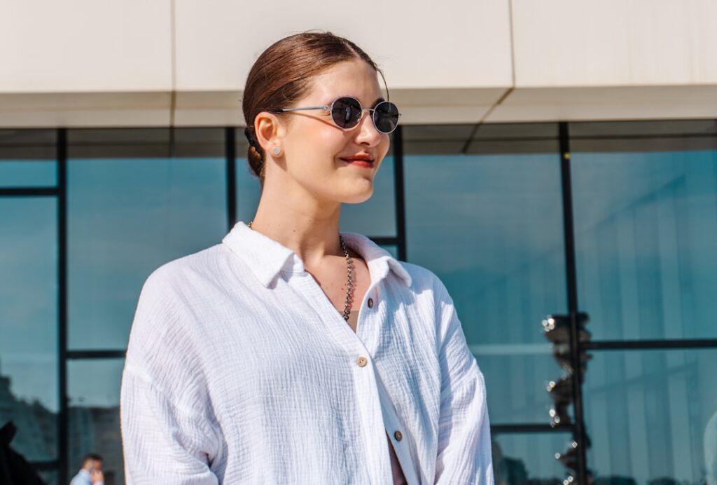 Young woman wearing sunglasses and white shirt outdoors.