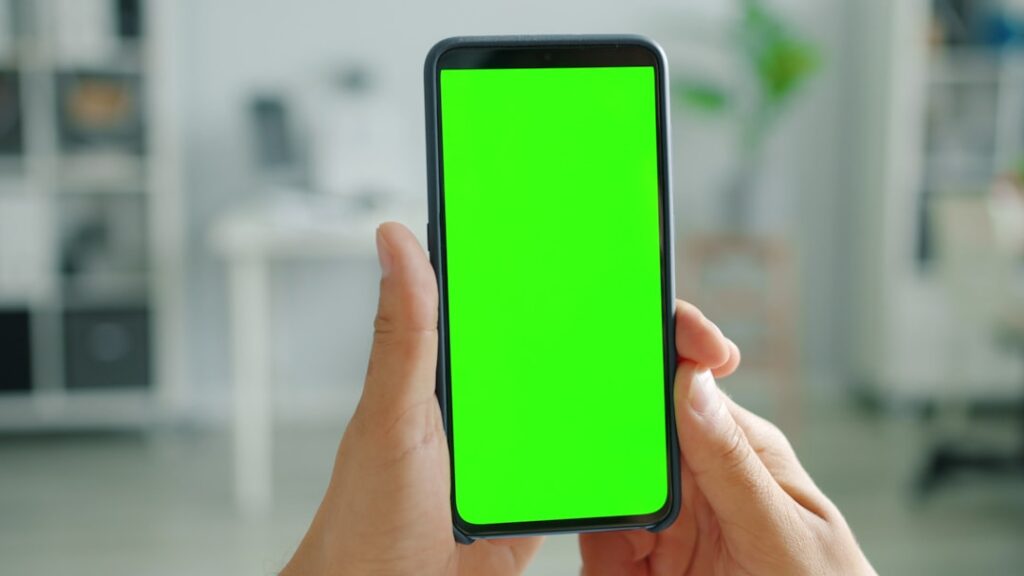 Person holding a smartphone with a green screen.