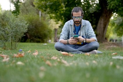 a man sitting in the grass looking at his cell phone