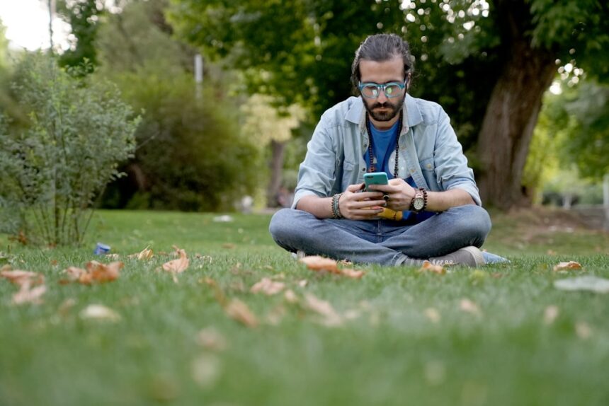 a man sitting in the grass looking at his cell phone