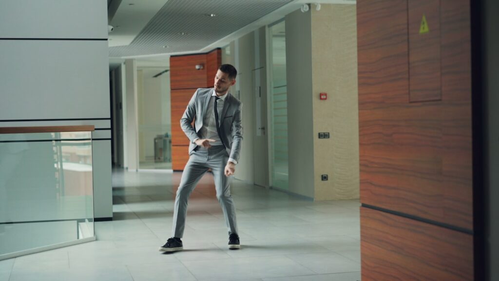 Man in suit dancing in modern office hallway.